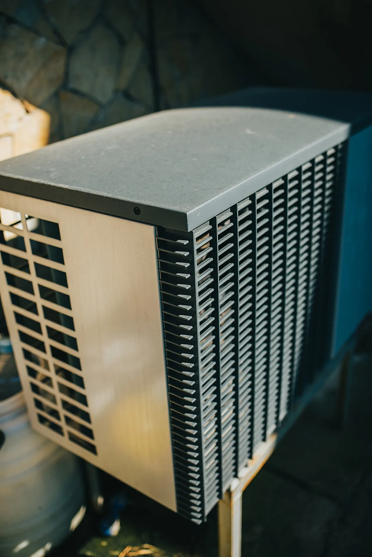 A residential outdoor air conditioning condenser unit beside a house, showing the finned coil that sheds heat.