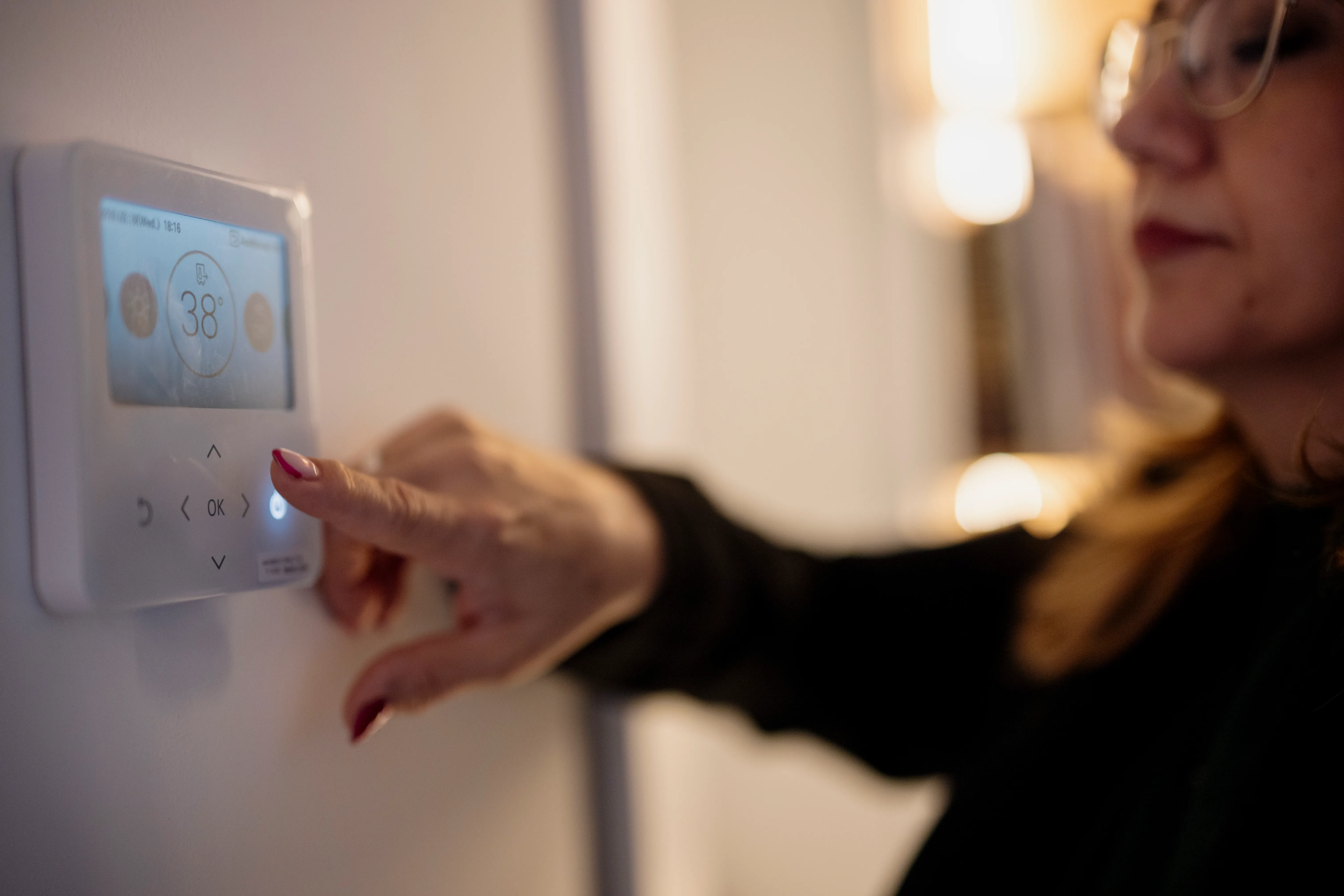 A homeowner setting the temperature on a wall-mounted digital thermostat.